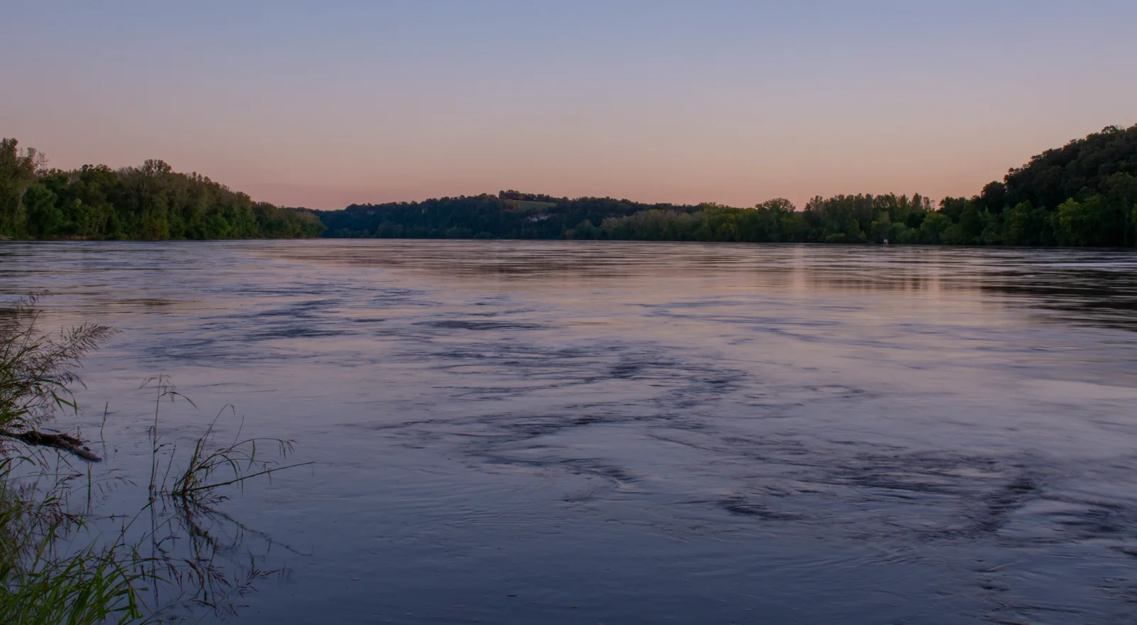 The Missouri River at dusk with bottomland timber and bluffs on the far bank