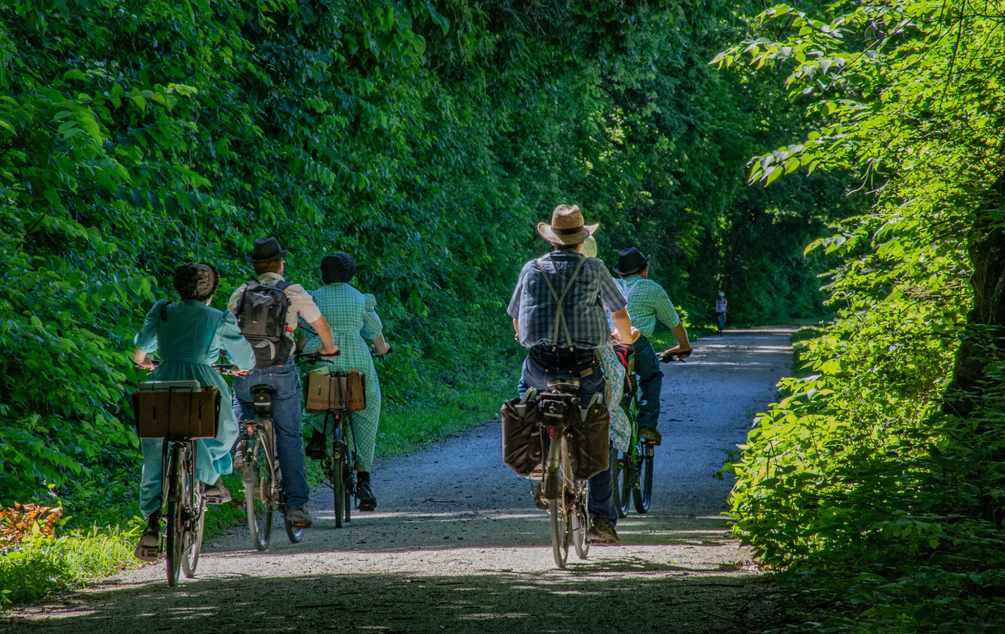Riders on the crushed-limestone Katy Trail under a green summer canopy near Boonville MO